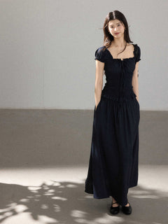 A woman in a black long dress with a square neckline, puff sleeves, and a ruffled waist.