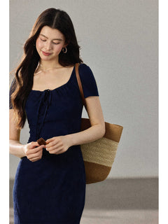 A close-up of a woman wearing a navy blue fitted dress with a square neckline and drawstring detail.