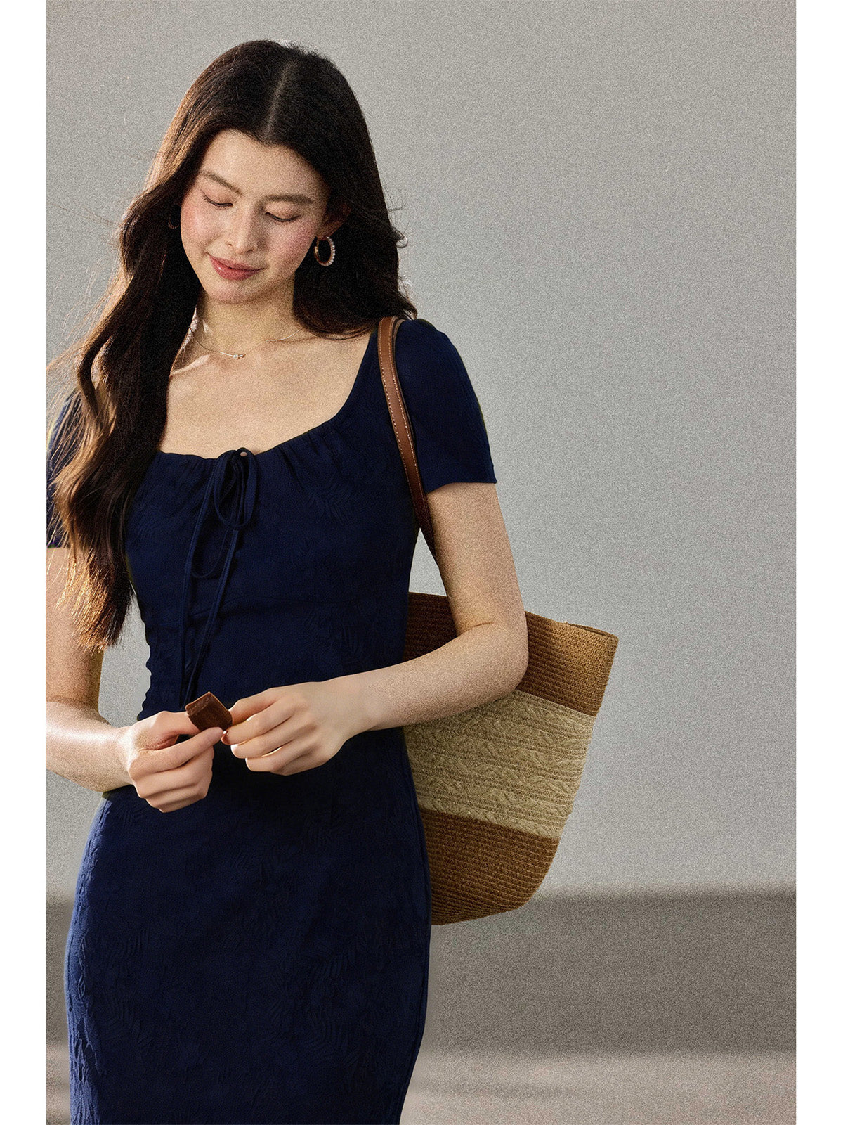 A close-up of a woman wearing a navy blue fitted dress with a square neckline and drawstring detail.
