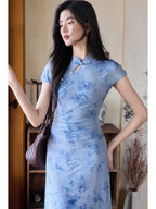 A woman in a light blue floral dress with a mandarin collar and keyhole opening, standing while holding a woven bag.