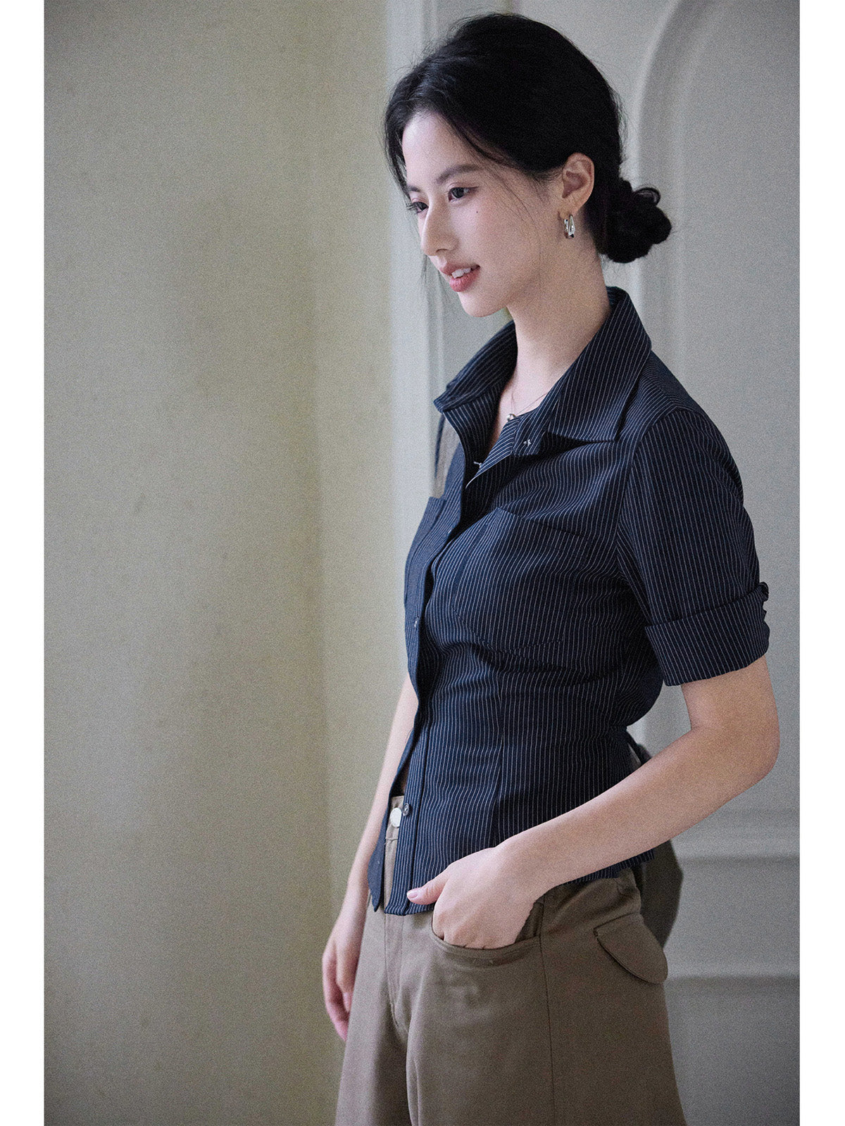 A woman wearing a navy striped fitted top with a collar, button-front closure, cuffed sleeves, and side ties.
