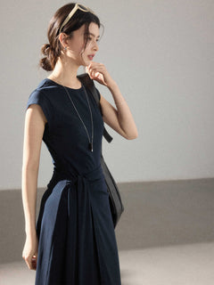 A woman in a navy blue dress with a round neckline, cap sleeves, and a waist tie.