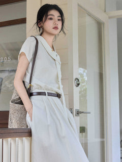 A woman wearing an ivory A-line long dress with a diagonal placket and brown belt.