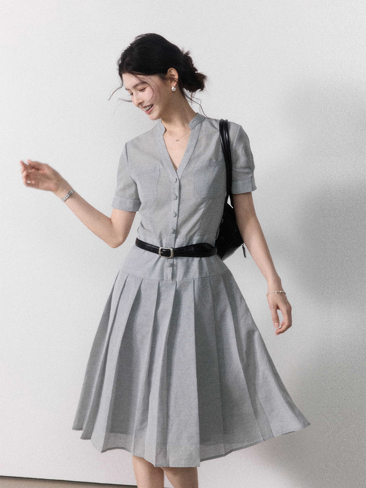 A woman in a grey A-line midi dress with short sleeves, a V-neck collar, and pleated skirt.