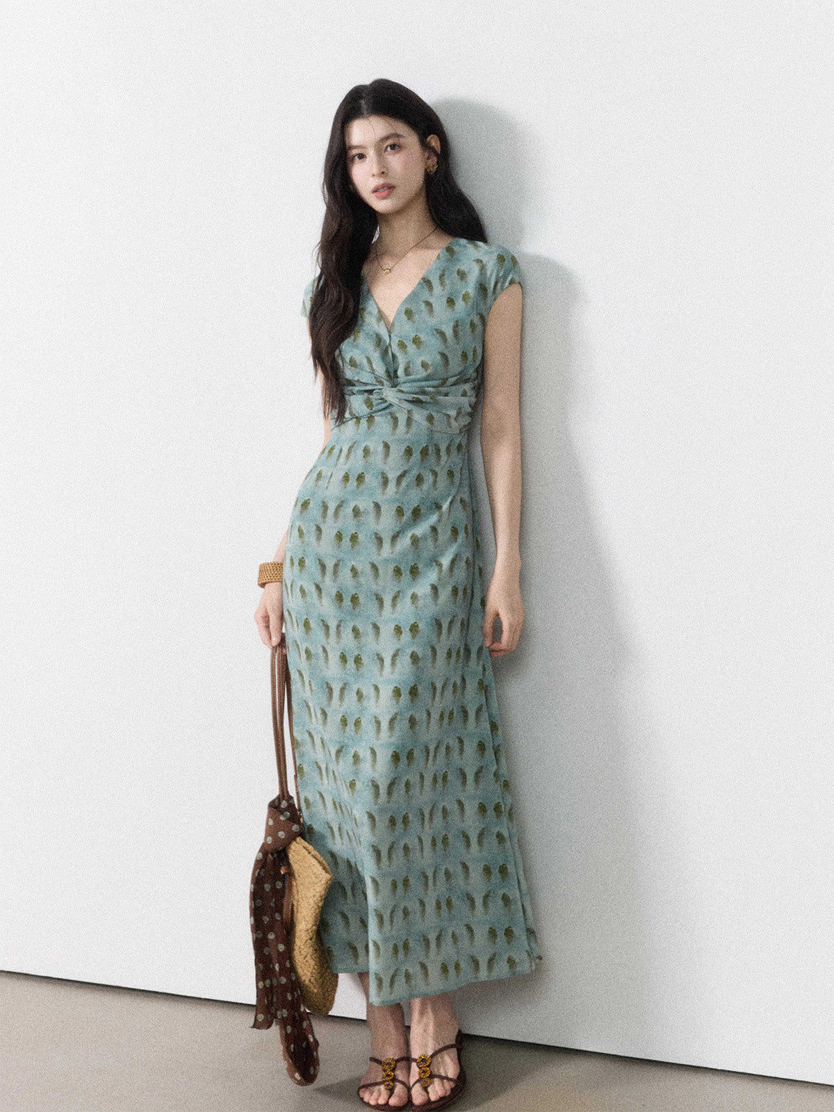 A woman in a long, light blue dress with a green leaf pattern and a back tie belt.