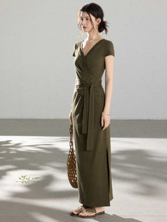 A woman in an olive green wrap dress with a V-neck and tie belt, standing.