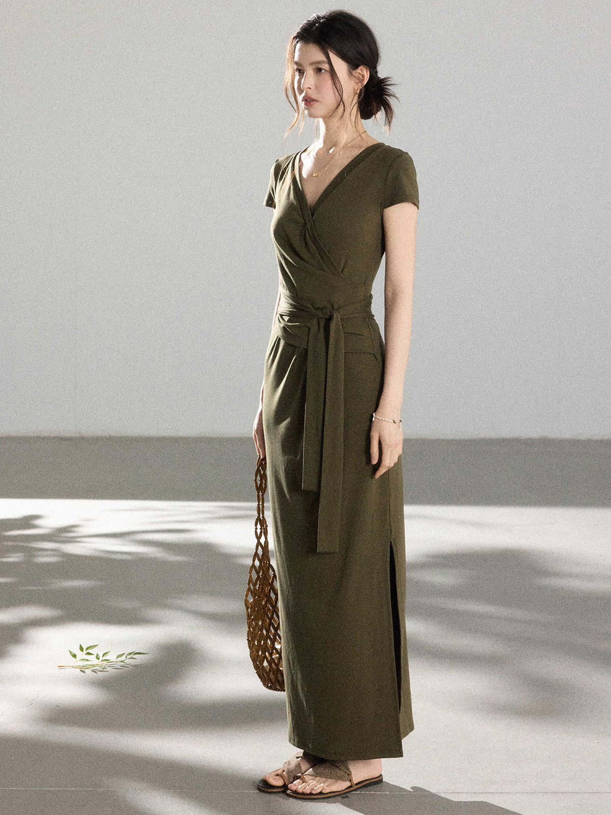 A woman in an olive green wrap dress with a V-neck and tie belt, standing.