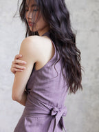 A close-up of the back of a purple sleeveless dress with a tied bow at the waist.