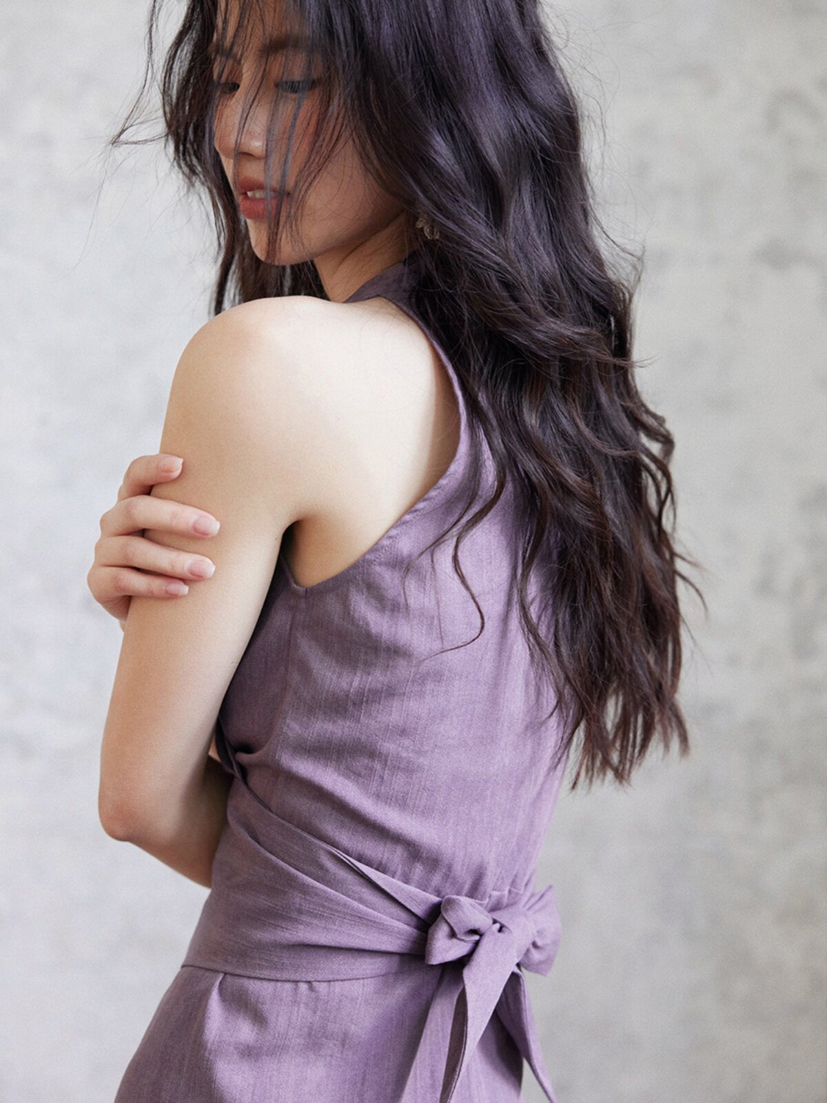 A close-up of the back of a purple sleeveless dress with a tied bow at the waist.
