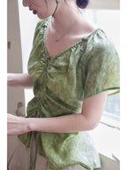 Close-up of a green tie-dye top featuring a V-neck and button details on the shoulder straps.