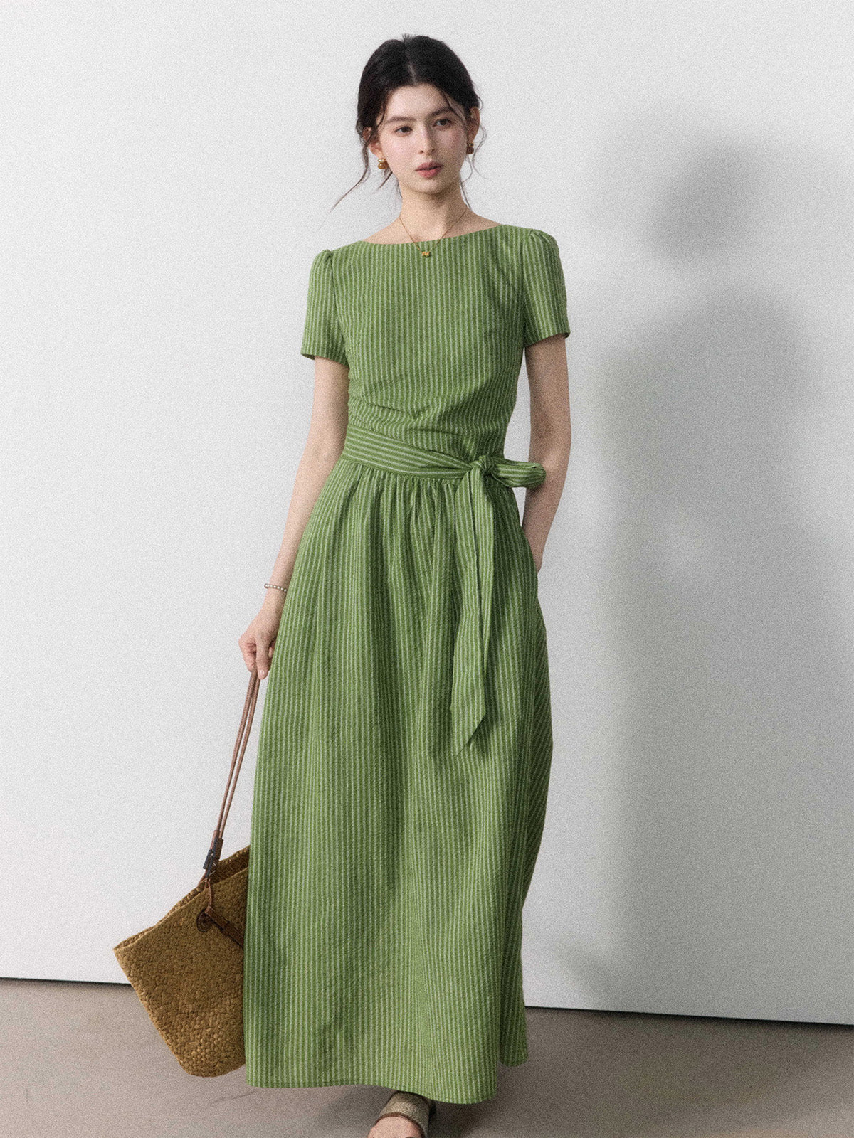 A woman wearing a sage green vertical-striped maxi dress with a tie belt.