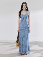 A woman in a light blue polka dot long slip dress with ruffled layers and an adjustable strap.