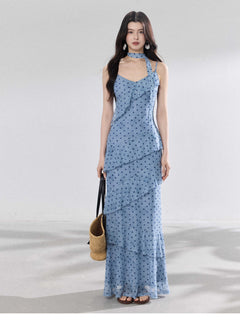 A woman in a light blue polka dot long slip dress with ruffled layers and an adjustable strap.