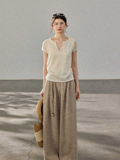 A woman stands in profile wearing a cream-colored knitted top with a V-neck and ribbed trim at the hem.