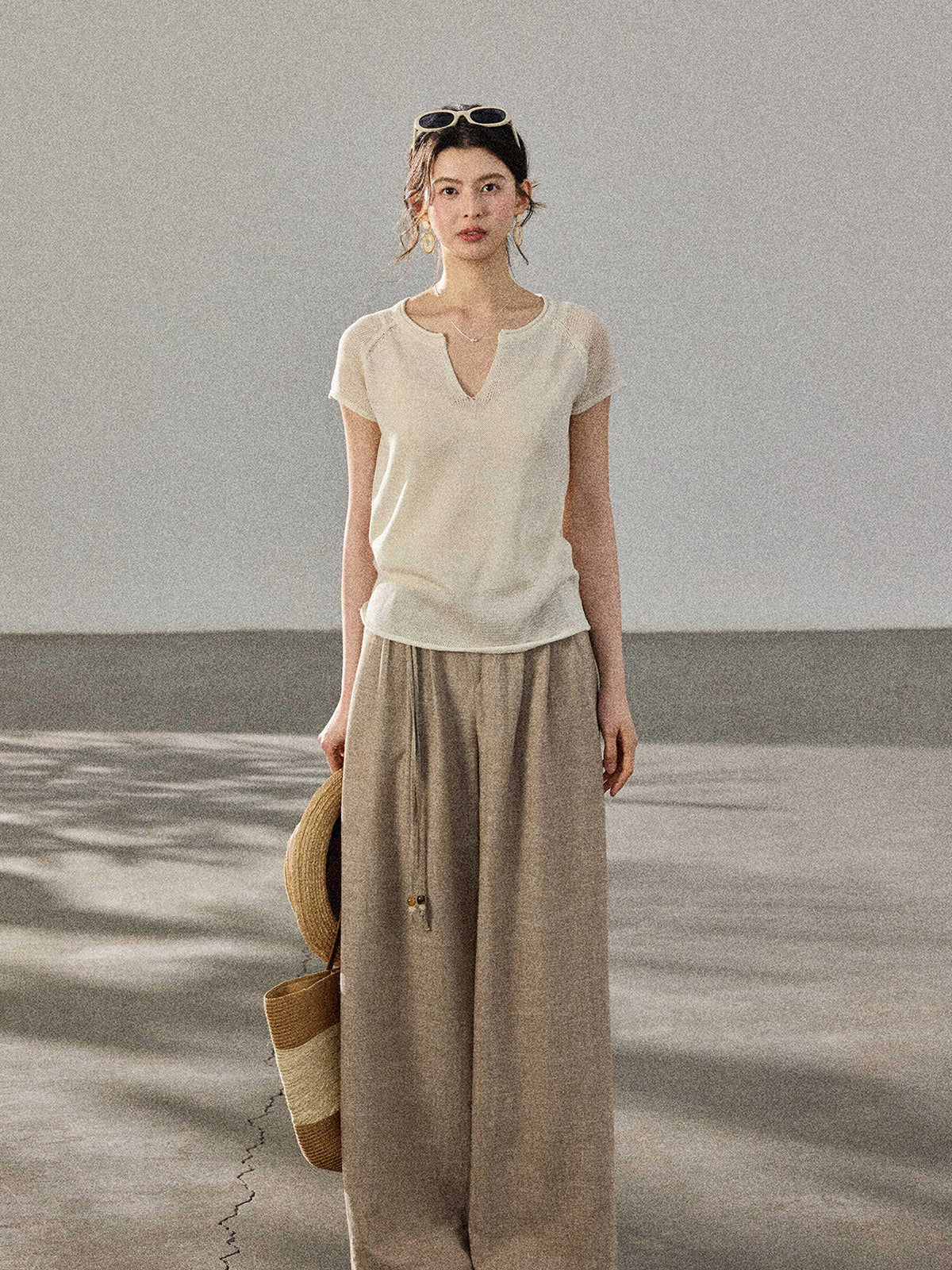 A woman stands in profile wearing a cream-colored knitted top with a V-neck and ribbed trim at the hem.