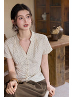 A woman wearing a cream polka dot short-sleeve top with a V-neck and button-front closure.