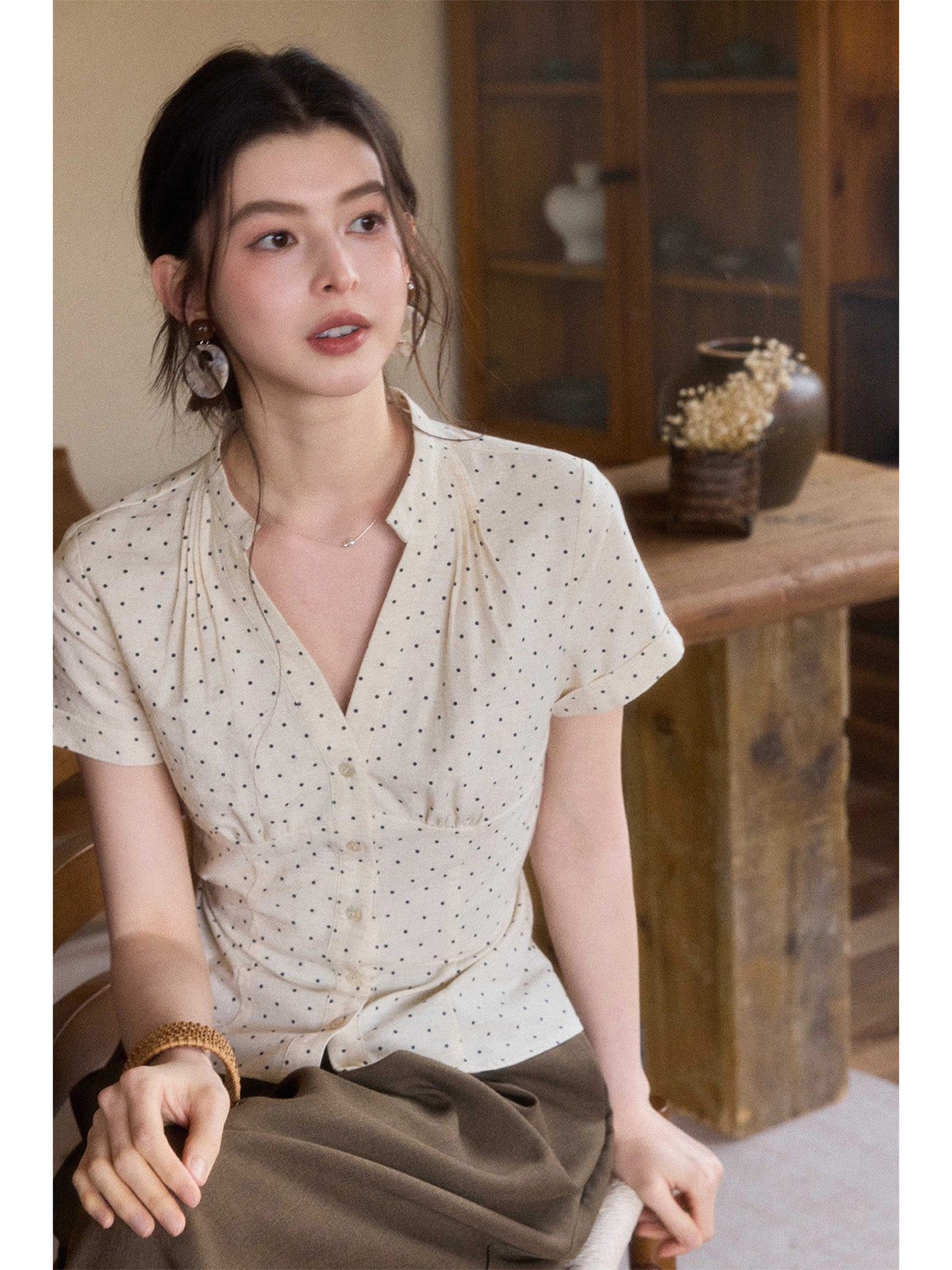 A woman wearing a cream polka dot short-sleeve top with a V-neck and button-front closure.
