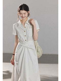 A woman wearing a white A-line dress with a button-front, collar, and twisted waist tie.