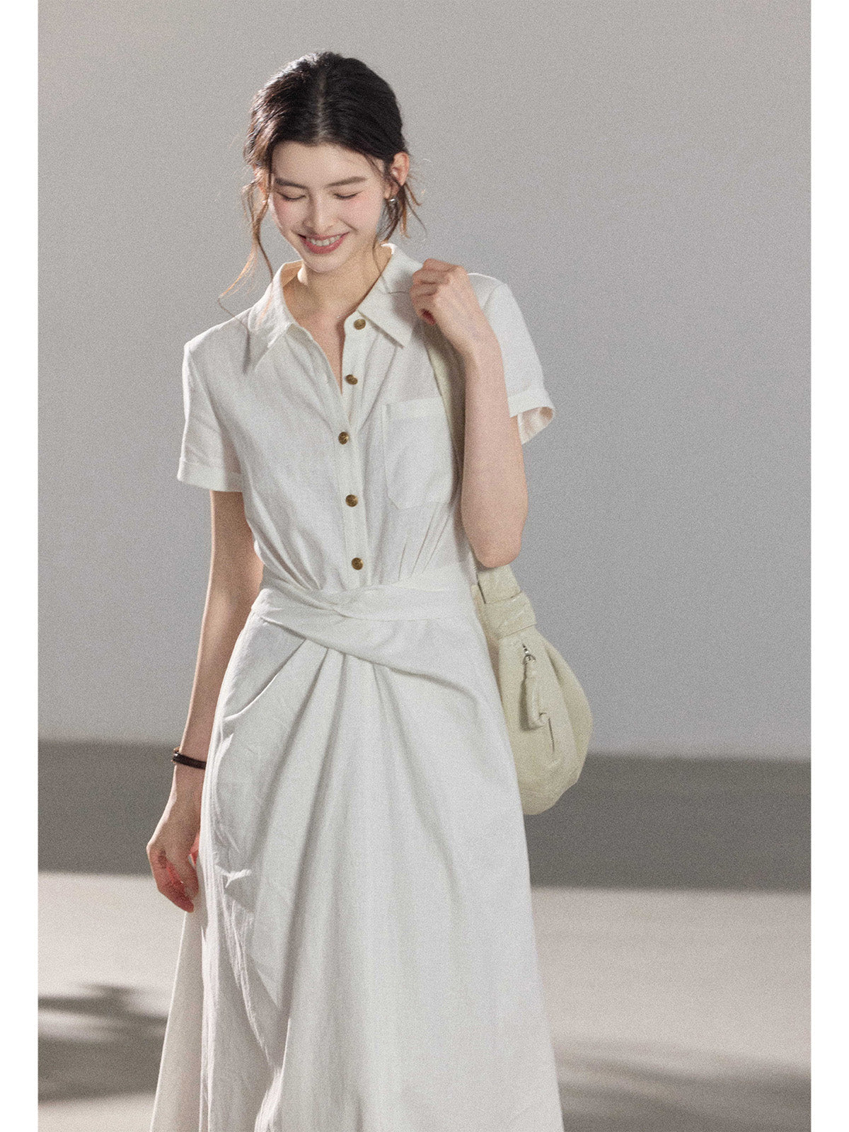 A woman wearing a white A-line dress with a button-front, collar, and twisted waist tie.