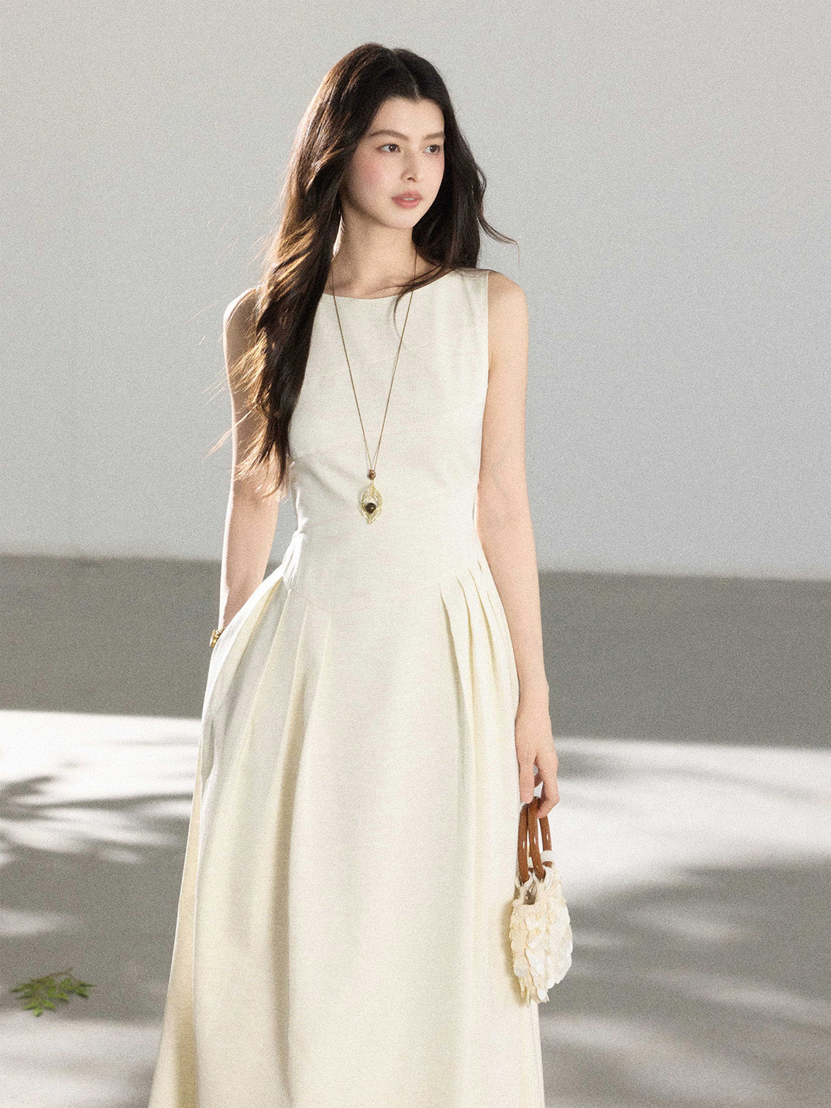 A woman in a cream sleeveless A-line floor-length dress with a round neckline and pleated skirt.