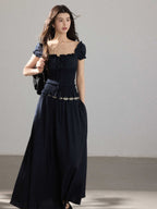 A woman in a black long dress with a square neckline, puff sleeves, and a smocked waist.