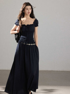 A woman in a black long dress with a square neckline, puff sleeves, and a smocked waist.