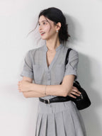 A woman in a grey A-line midi dress with short sleeves, a V-neck collar, and pleated skirt.