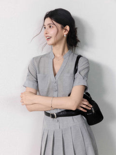 A woman in a grey A-line midi dress with short sleeves, a V-neck collar, and pleated skirt.