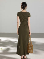 A woman in an olive green wrap dress with a V-neck and tie belt, seen from the back.