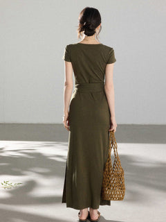 A woman in an olive green wrap dress with a V-neck and tie belt, seen from the back.