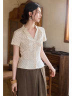 A woman wearing a cream polka dot short-sleeve top with a V-neck and button-front closure.