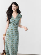 A woman in a long, light blue dress with a green leaf pattern and cap sleeves.