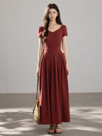 A woman in a red dress with a V-neck and front buttons, viewed from the side.