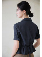 A woman wearing a navy striped fitted top with a collar, button-front closure, cuffed sleeves, and side ties.