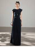 A woman wearing a navy blue long dress with a side pleat detail and an asymmetrical hem.