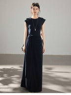 A woman wearing a navy blue long dress with a side pleat detail and an asymmetrical hem.