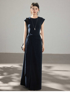 A woman wearing a navy blue long dress with a side pleat detail and an asymmetrical hem.