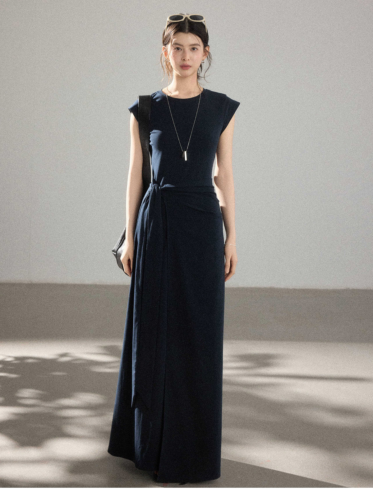 A woman wearing a navy blue long dress with a side pleat detail and an asymmetrical hem.