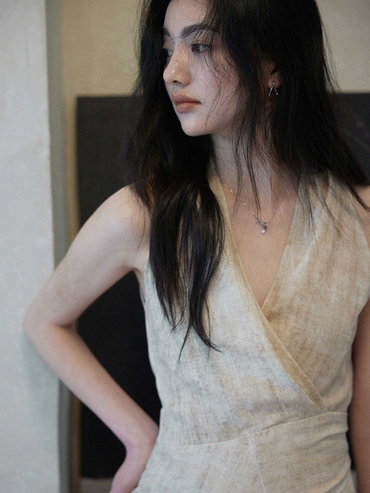 A close-up of a woman's face wearing a beige wrap dress with a V-neck and asymmetrical hemline.