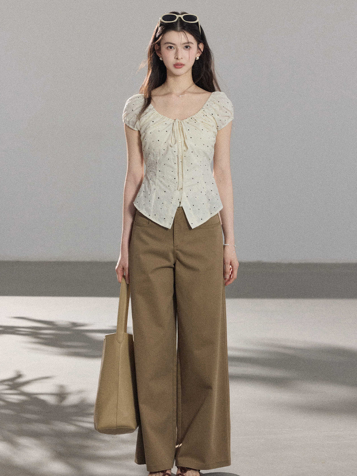A woman wearing a cream polka dot top with puff sleeves, paired with brown wide-leg pants.