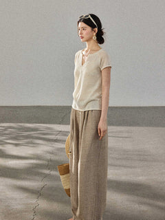 A woman stands in profile wearing a cream-colored knitted top with a V-neck and ribbed trim at the hem.
