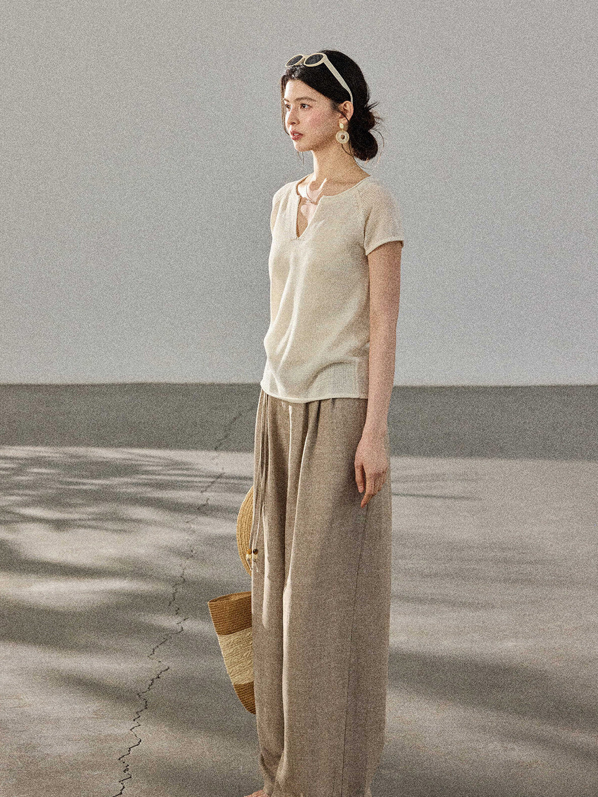 A woman stands in profile wearing a cream-colored knitted top with a V-neck and ribbed trim at the hem.