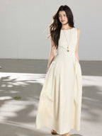 A woman in a cream sleeveless A-line floor-length dress with a round neckline and pleated skirt.