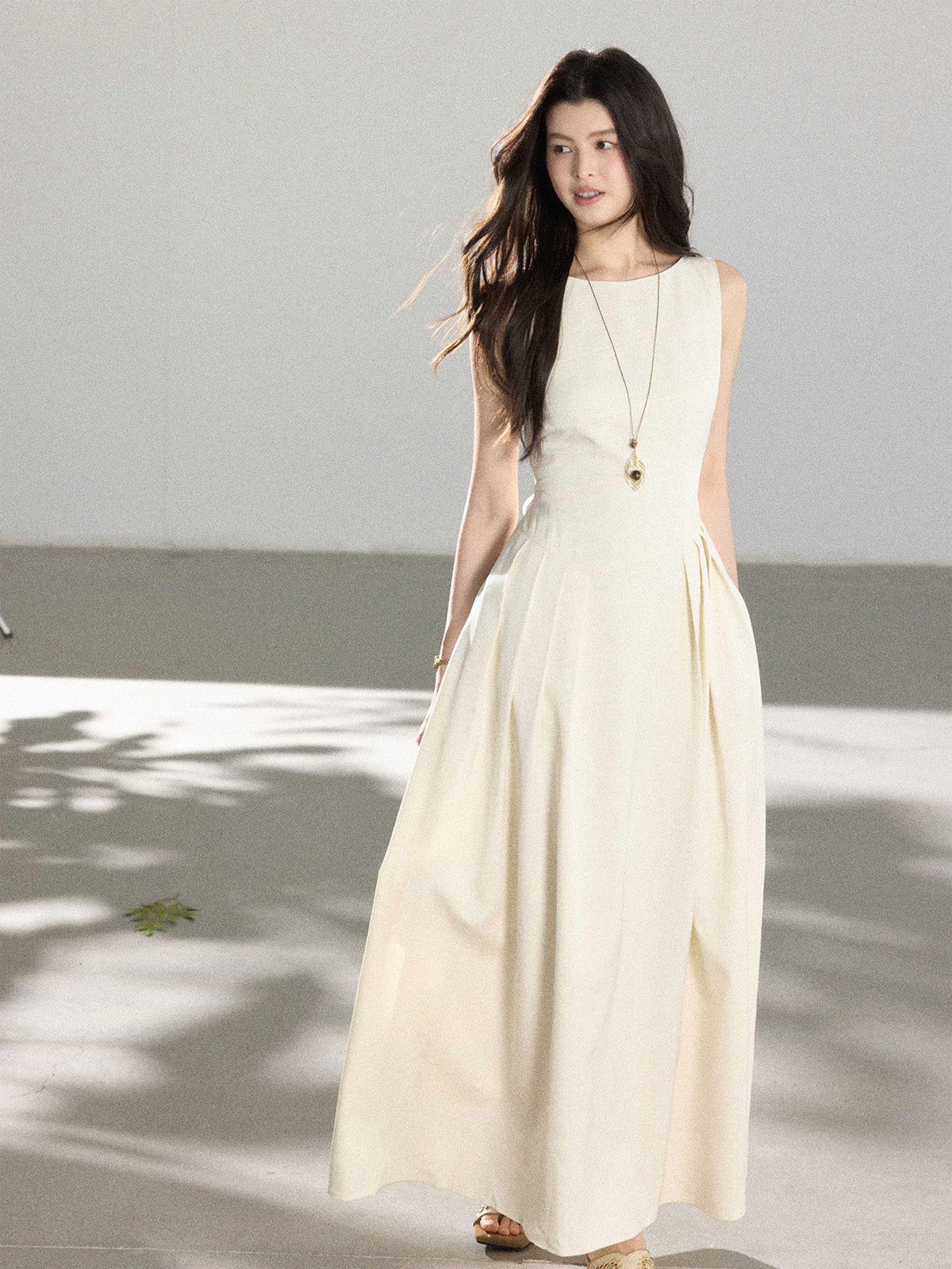 A woman in a cream sleeveless A-line floor-length dress with a round neckline and pleated skirt.