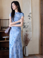 A woman in a light blue floral dress with a mandarin collar and keyhole opening, standing with her arms crossed.