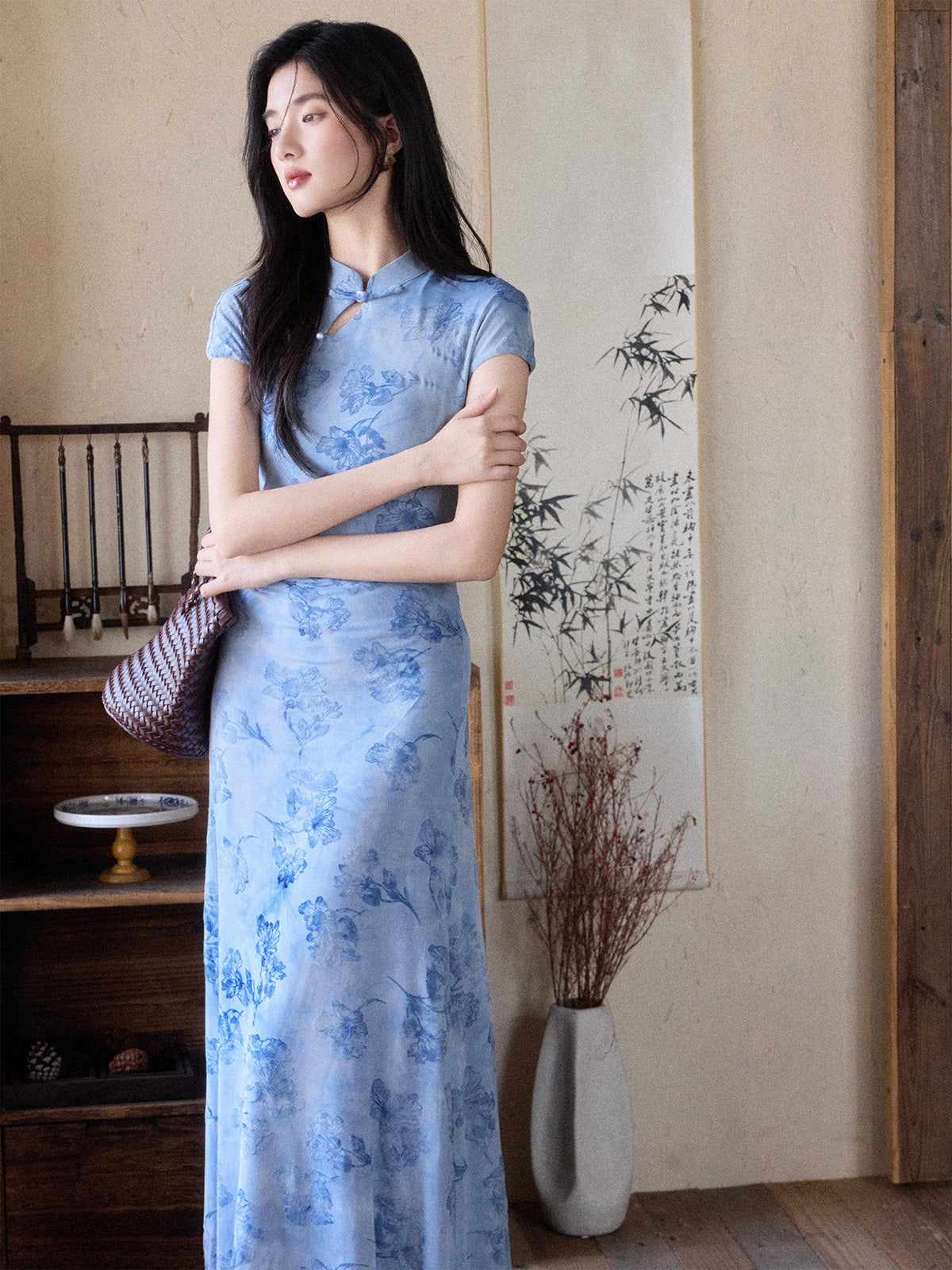 A woman in a light blue floral dress with a mandarin collar and keyhole opening, standing with her arms crossed.
