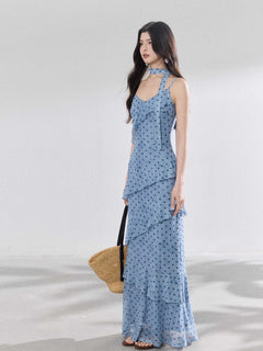 A woman in a light blue polka dot long slip dress with ruffled layers and an adjustable strap.