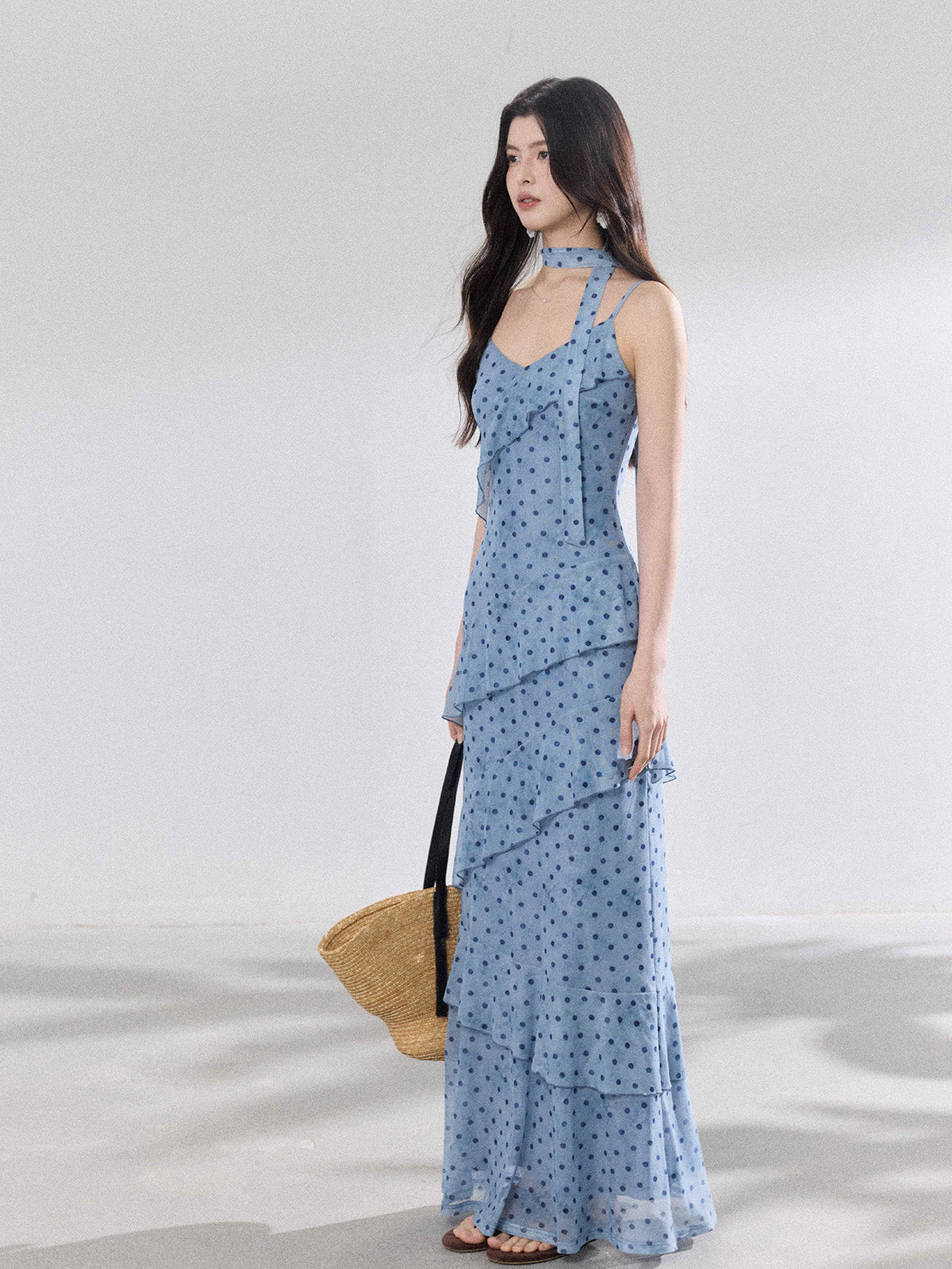 A woman in a light blue polka dot long slip dress with ruffled layers and an adjustable strap.