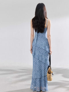 A woman in a light blue polka dot long slip dress with ruffled layers and an adjustable strap.