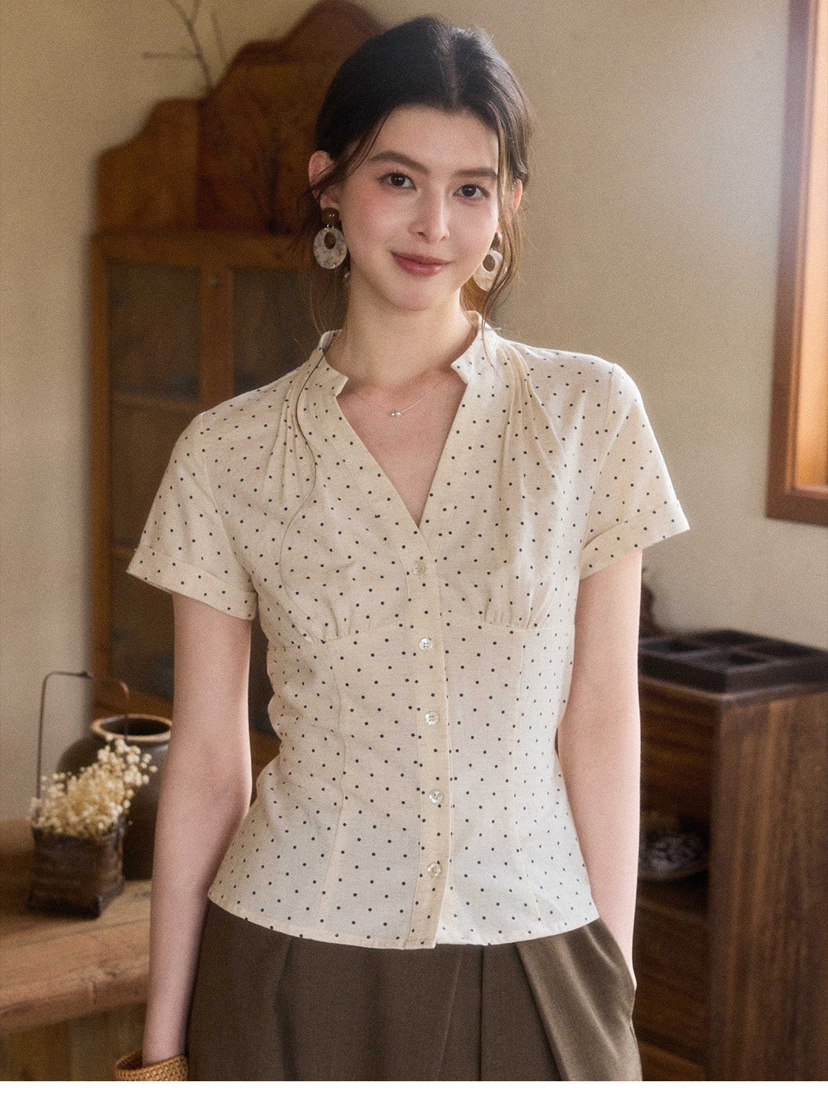 A woman wearing a cream polka dot short-sleeve top with a V-neck and button-front closure.